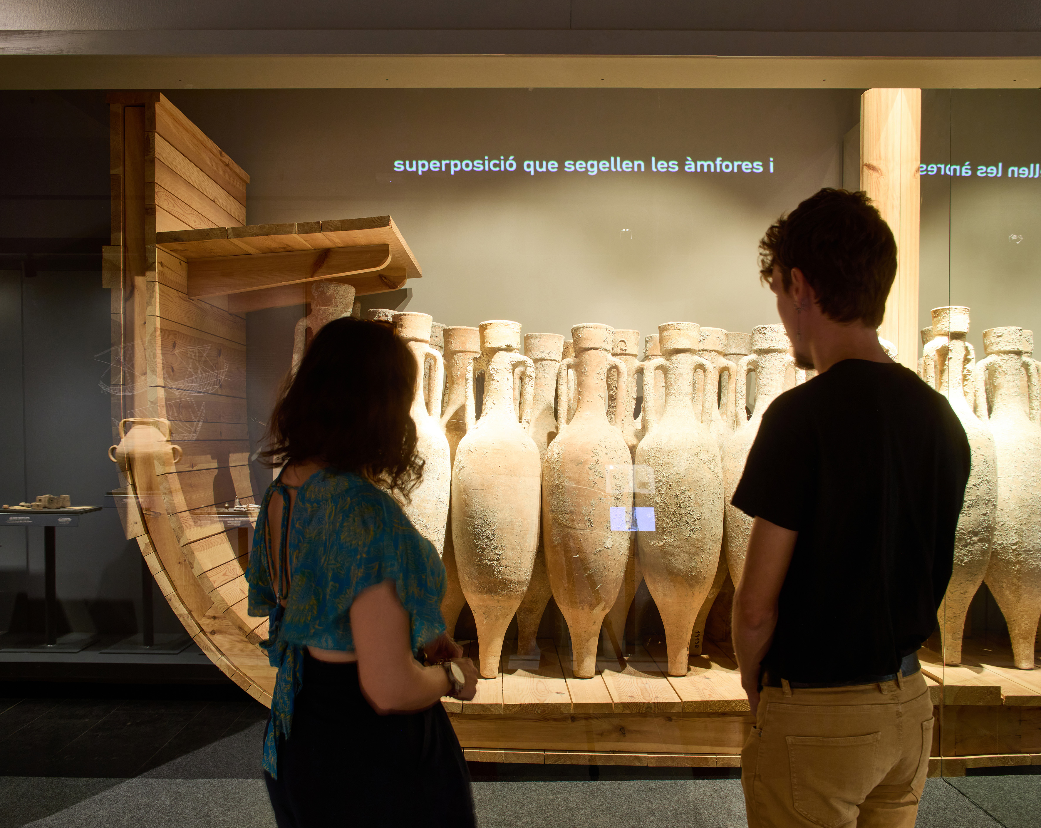 Dos persones d'esquenes mirant una vitrina amb àmfores.