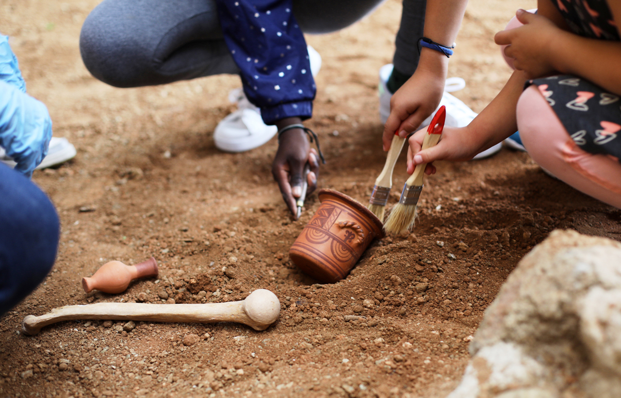 Tres infants excavant rèpliques de peces arqueològiques.