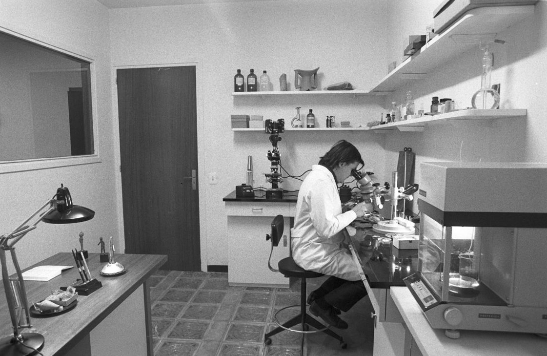 Fotografia antiga d'una científica mirant per un microscopi en un laboratori.